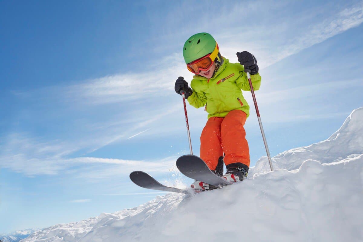 boy skiing with bright orange pants and yellow jacket and helmet