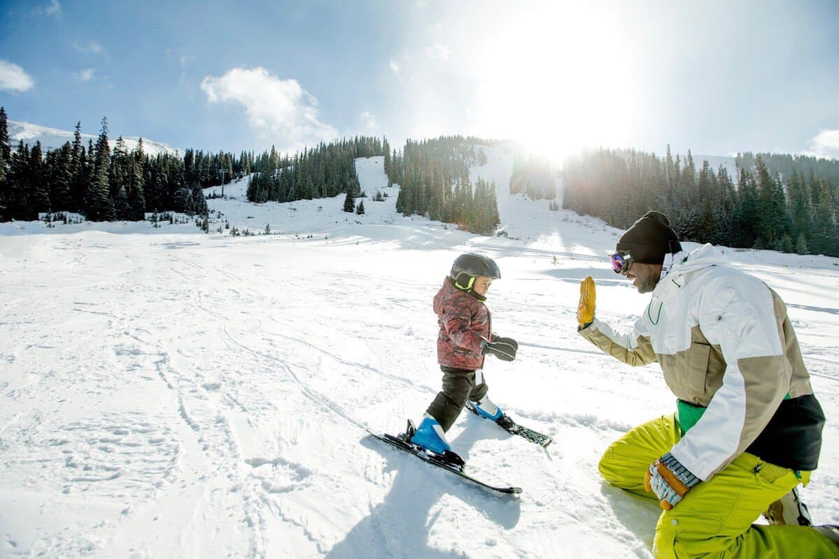 Happy father giving high five while teaching his young son to ski during winter.