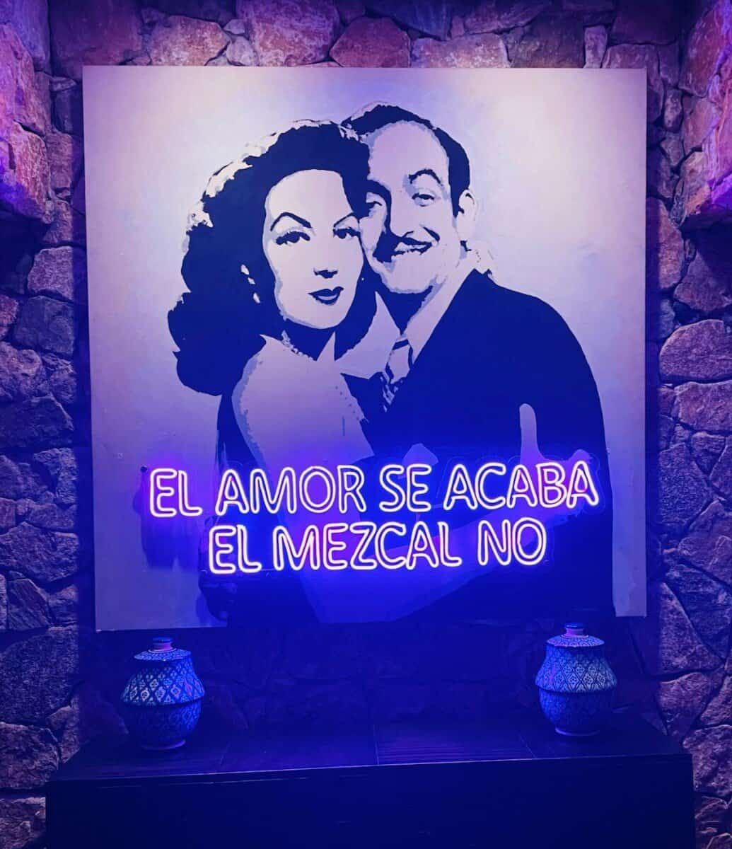 portrait of a woman and man with 'el amor se acaba el mezcal no' written on it in florescent lights