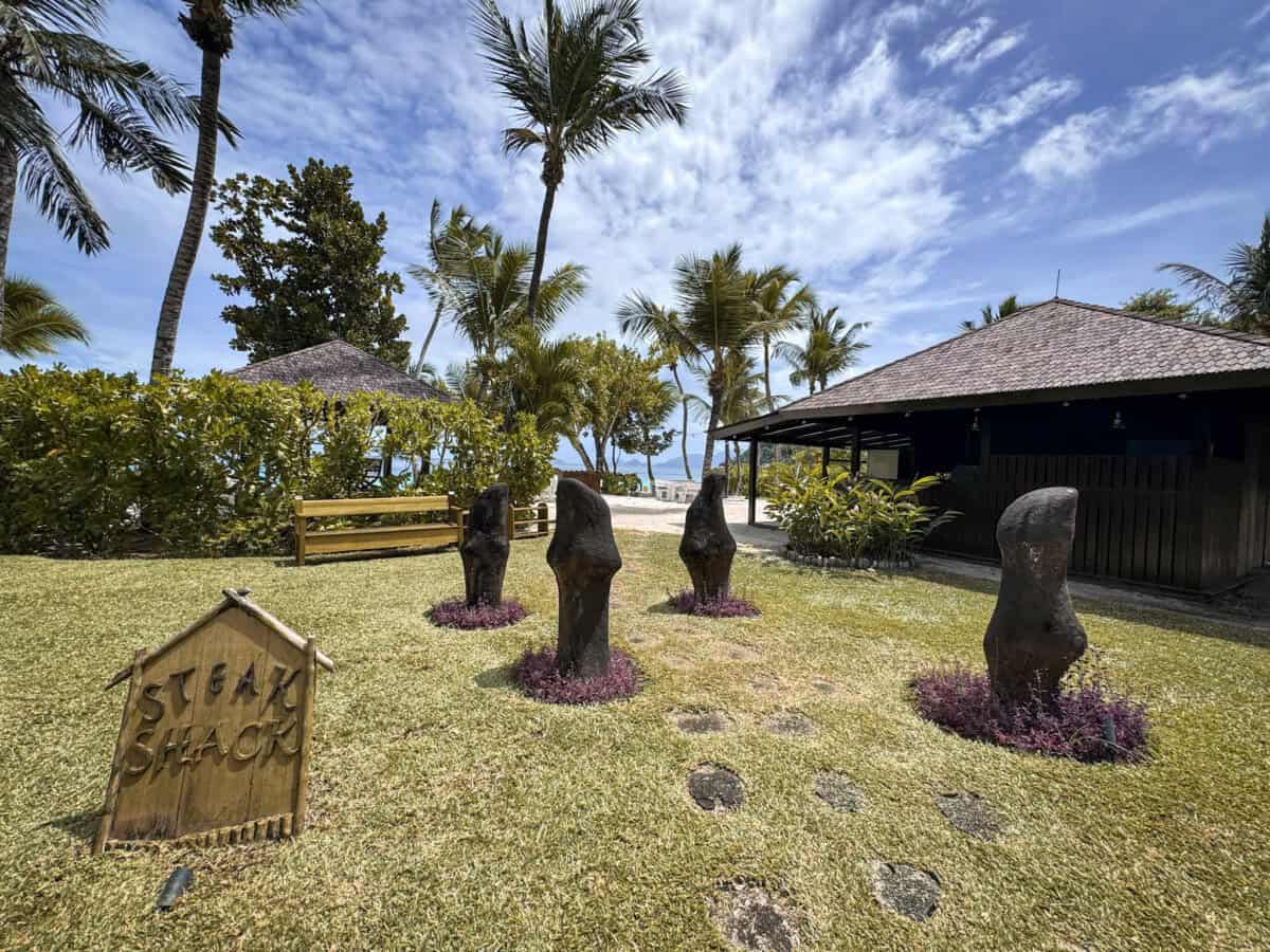 grassy field with palm trees and blue skies and sign saying steak shack at Four Seasons Seychelles Resorts