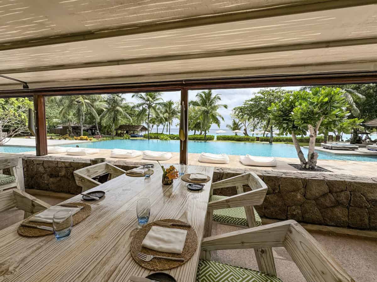 outdoor living space with tables and chairs and a pool in the backdrop at Four Seasons Seychelles Resorts