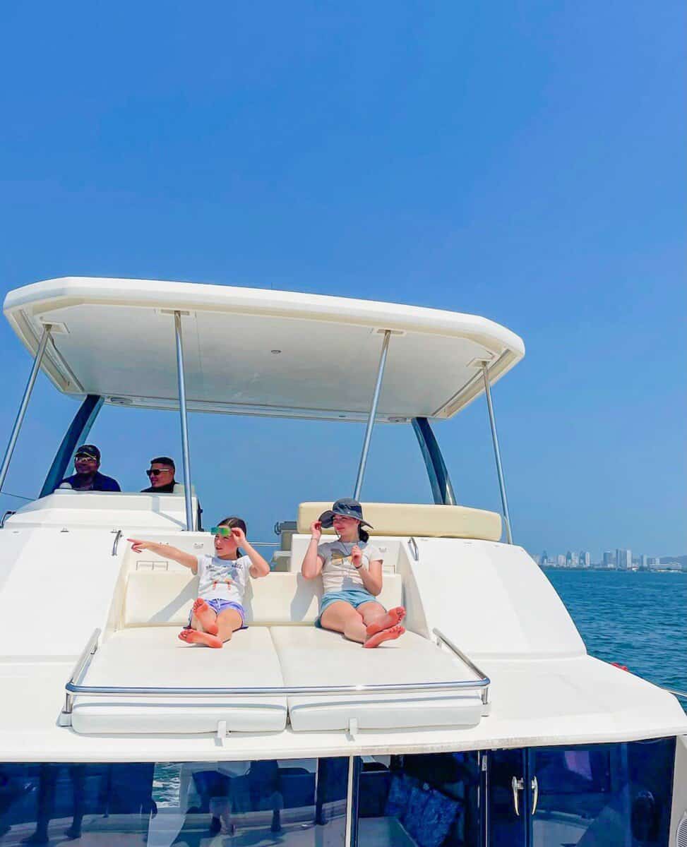 two children sitting on back of boat with blue skies