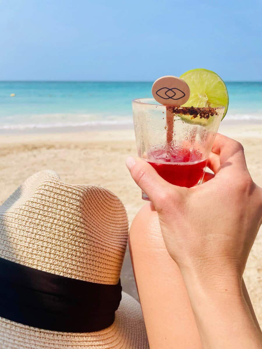 woman holding drink in front of white sand beach with turquoise blue waters in Cartagena, Colombia